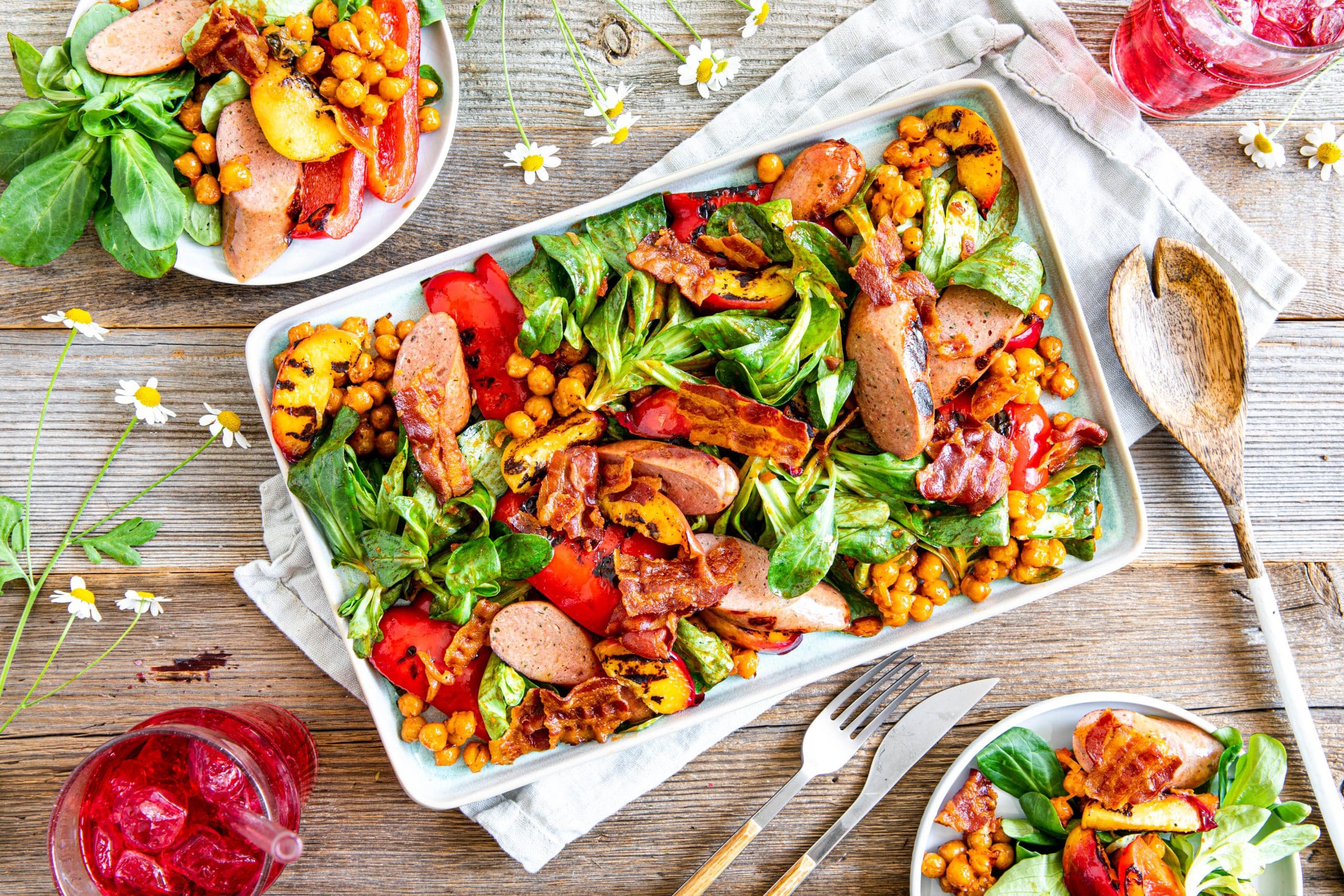 Geflügelwurst mit Bacon auf buntem Grillsalat mit Kichererbsen
